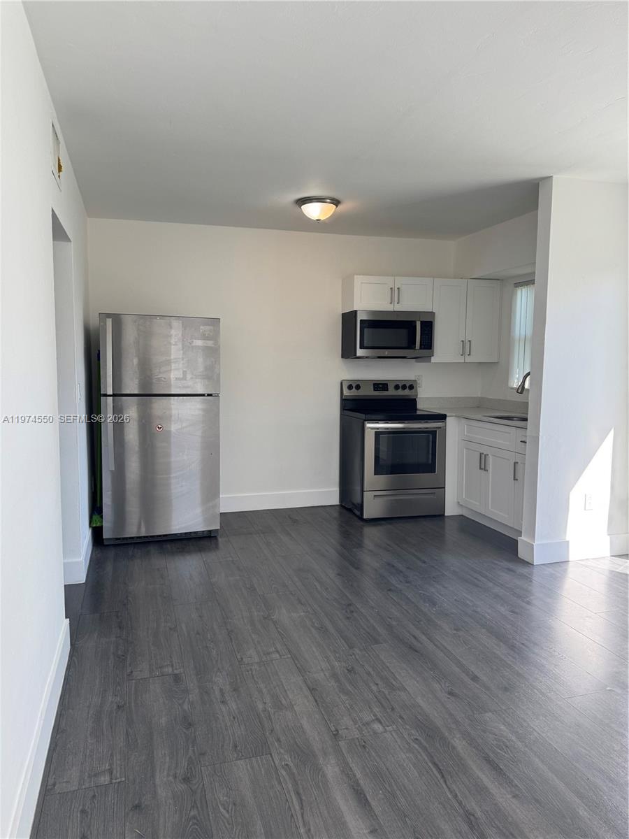 A kitchen features stainless steel appliances, white cabinets, and dark wood-look flooring — 2150 NW 24th St, Miami FL 33142, MIAMI, FL