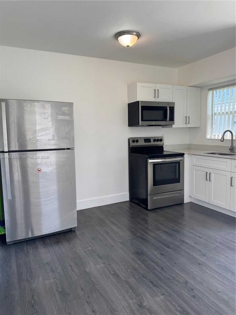 This kitchen features stainless steel appliances, white cabinets, and dark wood-look flooring — 2150 NW 24th St, Miami FL 33142, MIAMI, FL