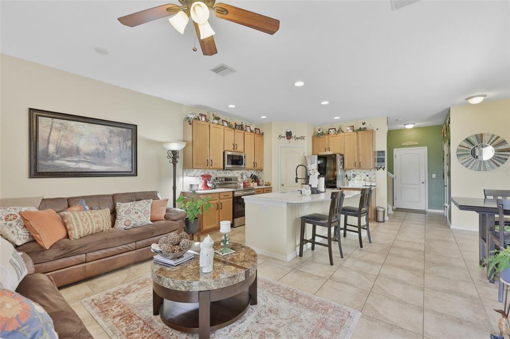 An open-concept living room and kitchen featuring a brown sofa, island, and tile flooring — 8718 TURNSTONE HAVEN PLACE, TAMPA, FL