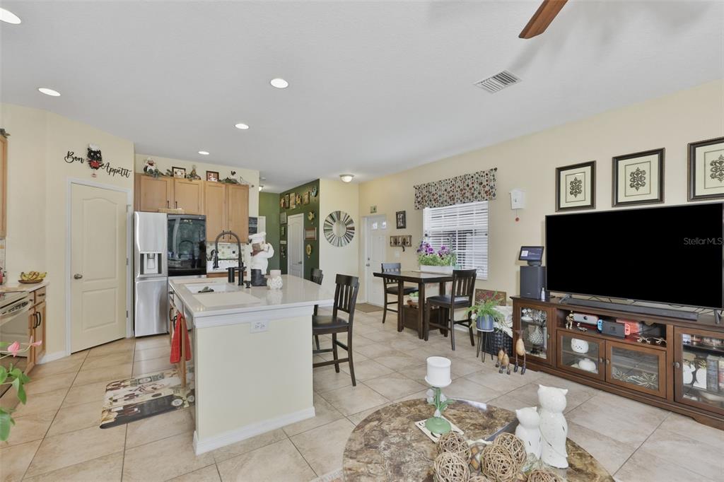 An open-concept kitchen and living area features tile flooring, a center island, and a television — 8718 TURNSTONE HAVEN PLACE, TAMPA, FL