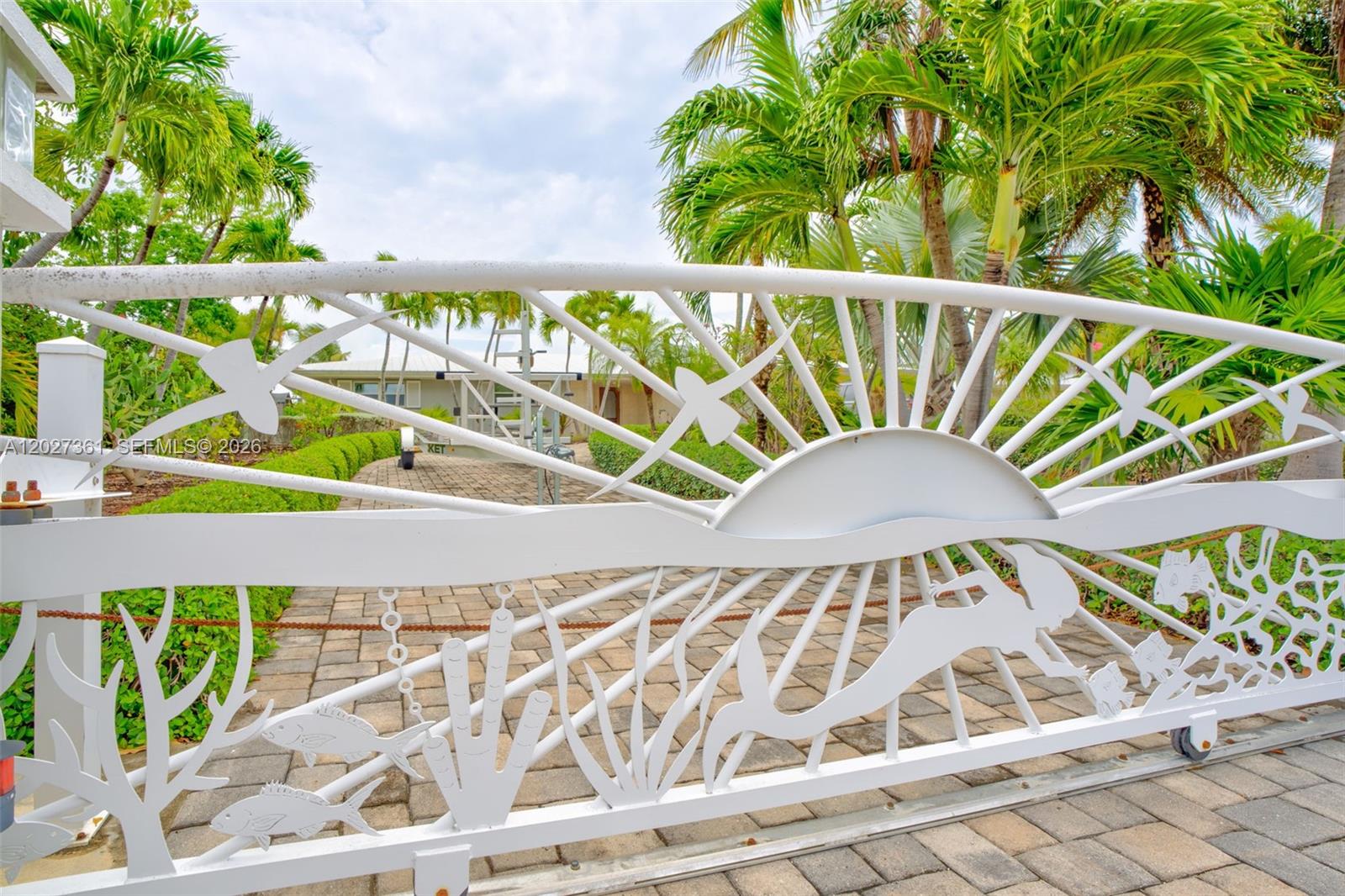 A decorative white metal gate features a sun, mermaid, and fish design at an entrance — 2919 Sombrero Blvd, Key Largo FL 33050, KEY LARGO, FL