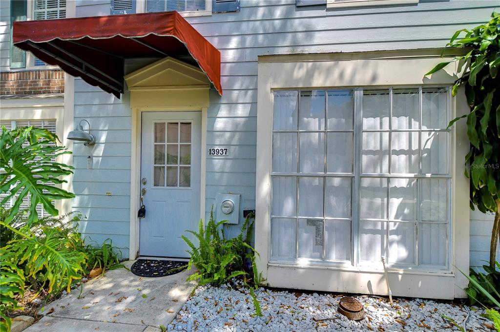 The exterior of a light blue home features a red awning over the front door — 13937 FLETCHERS MILL DRIVE, TAMPA, FL