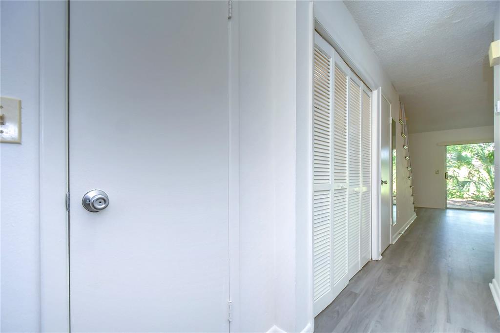 A hallway with light wood-look flooring, white walls, and white louvered closet doors — 13937 FLETCHERS MILL DRIVE, TAMPA, FL