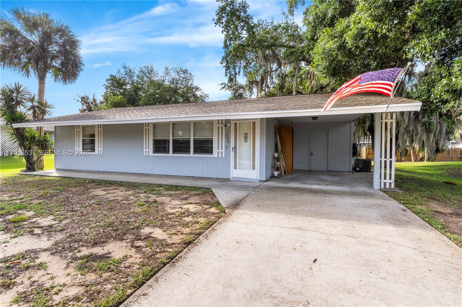 A single-story light blue house with a carport and an American flag in the front — 326 Belfast, Sebastian FL 32958, SEBASTIAN, FL