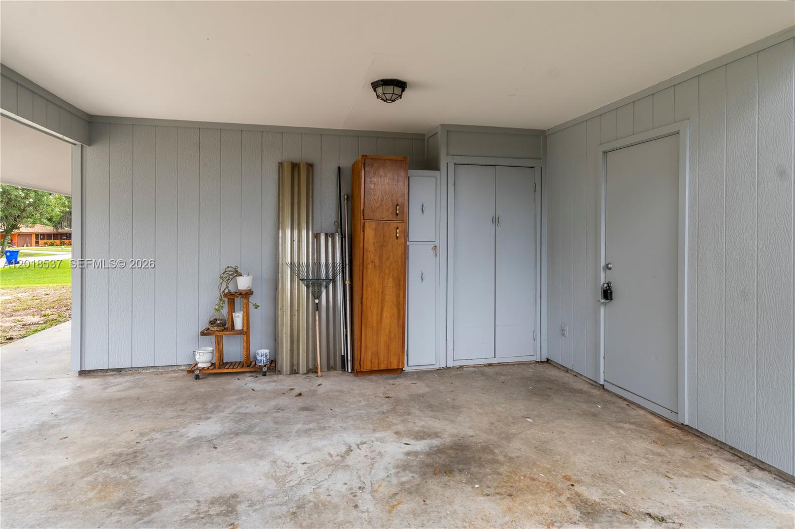 A covered carport features light gray paneled walls, a concrete floor, and built-in storage cabinets — 326 Belfast, Sebastian FL 32958, SEBASTIAN, FL