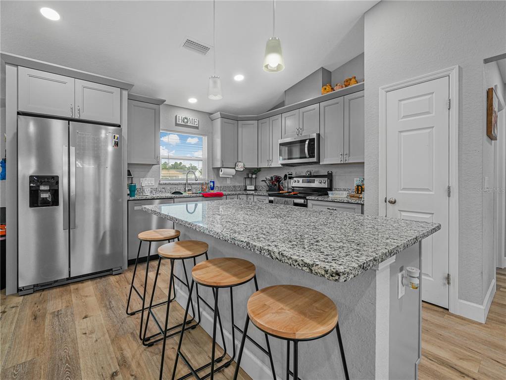 A kitchen features gray cabinets, granite countertops, a stainless steel refrigerator, and three bar stools — 346 HIDDEN CREEK, WAUCHULA, FL