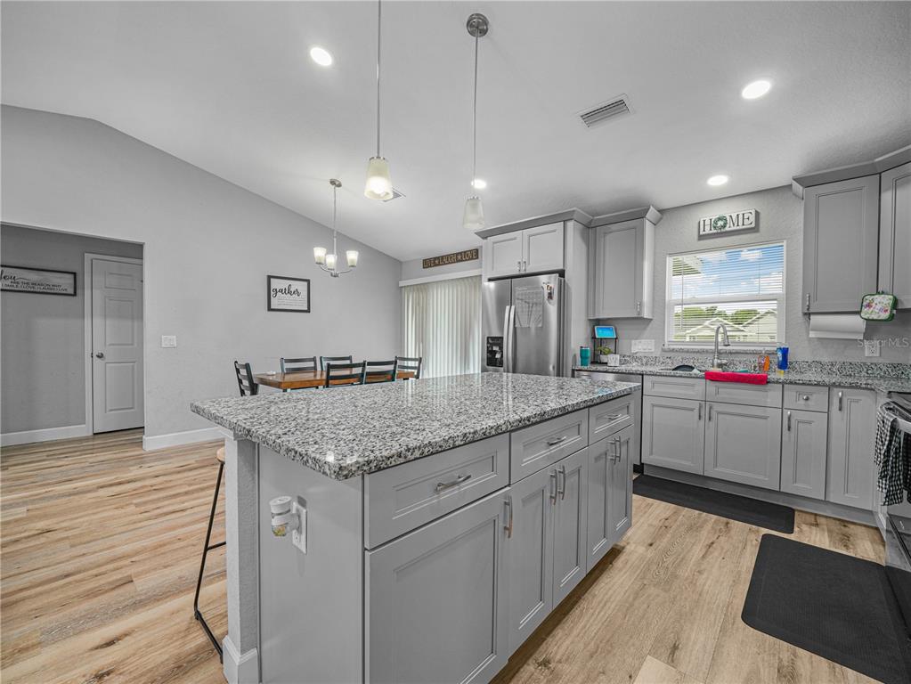 A kitchen features a granite-topped island, gray cabinetry, and light wood-look flooring — 346 HIDDEN CREEK, WAUCHULA, FL