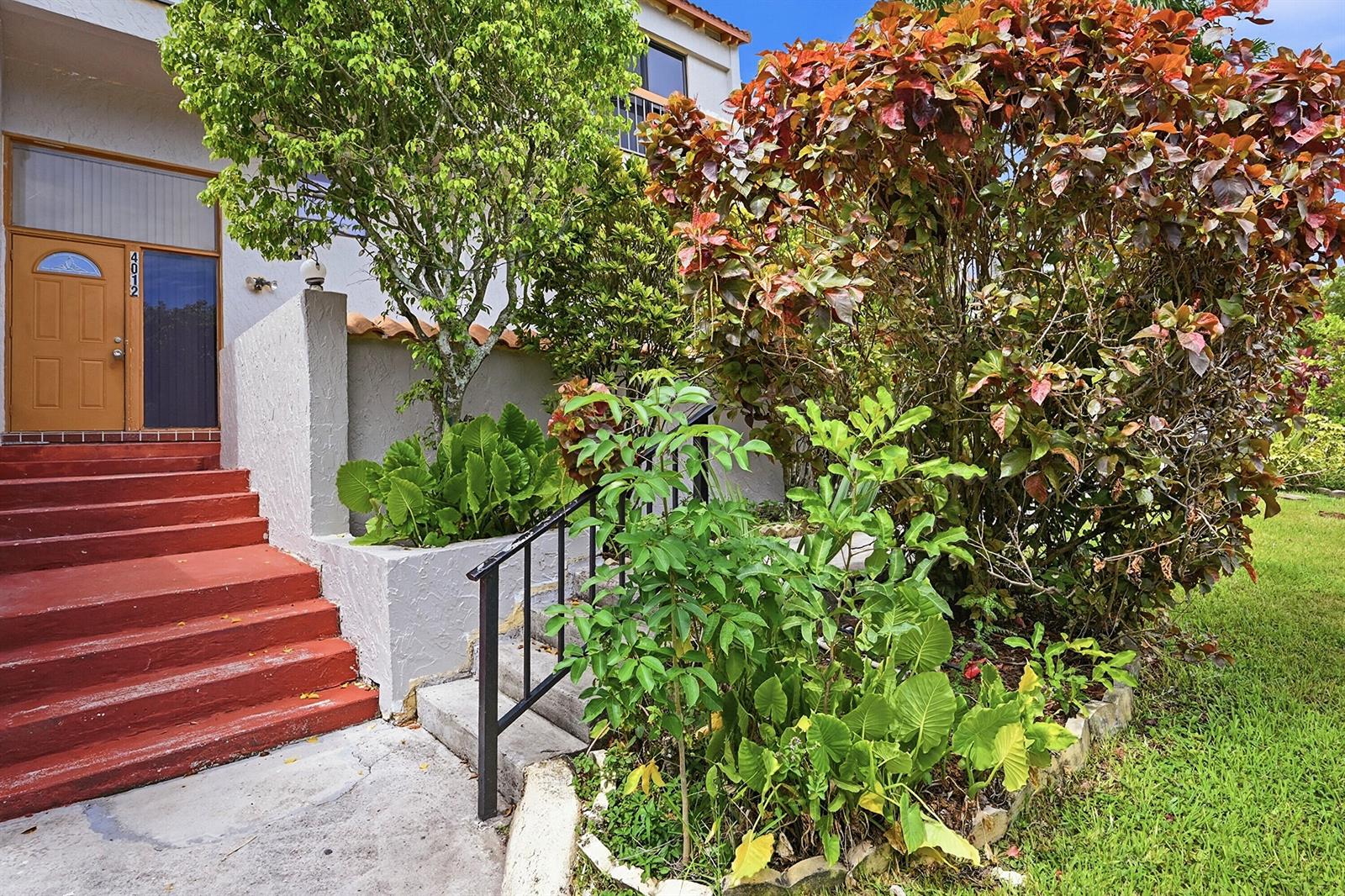 A house entrance features red stairs leading to a wooden door next to lush landscaping — 4012 Del Rio Way, Sunrise FL 33351, SUNRISE, FL