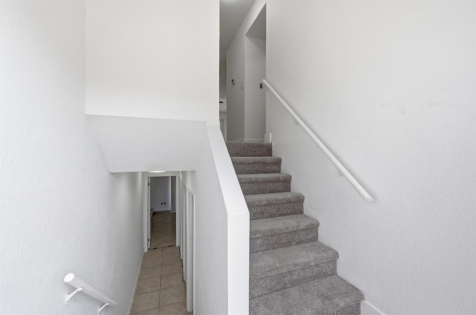 A staircase with gray carpet leads upward between white walls next to a lower hallway — 4012 Del Rio Way, Sunrise FL 33351, SUNRISE, FL