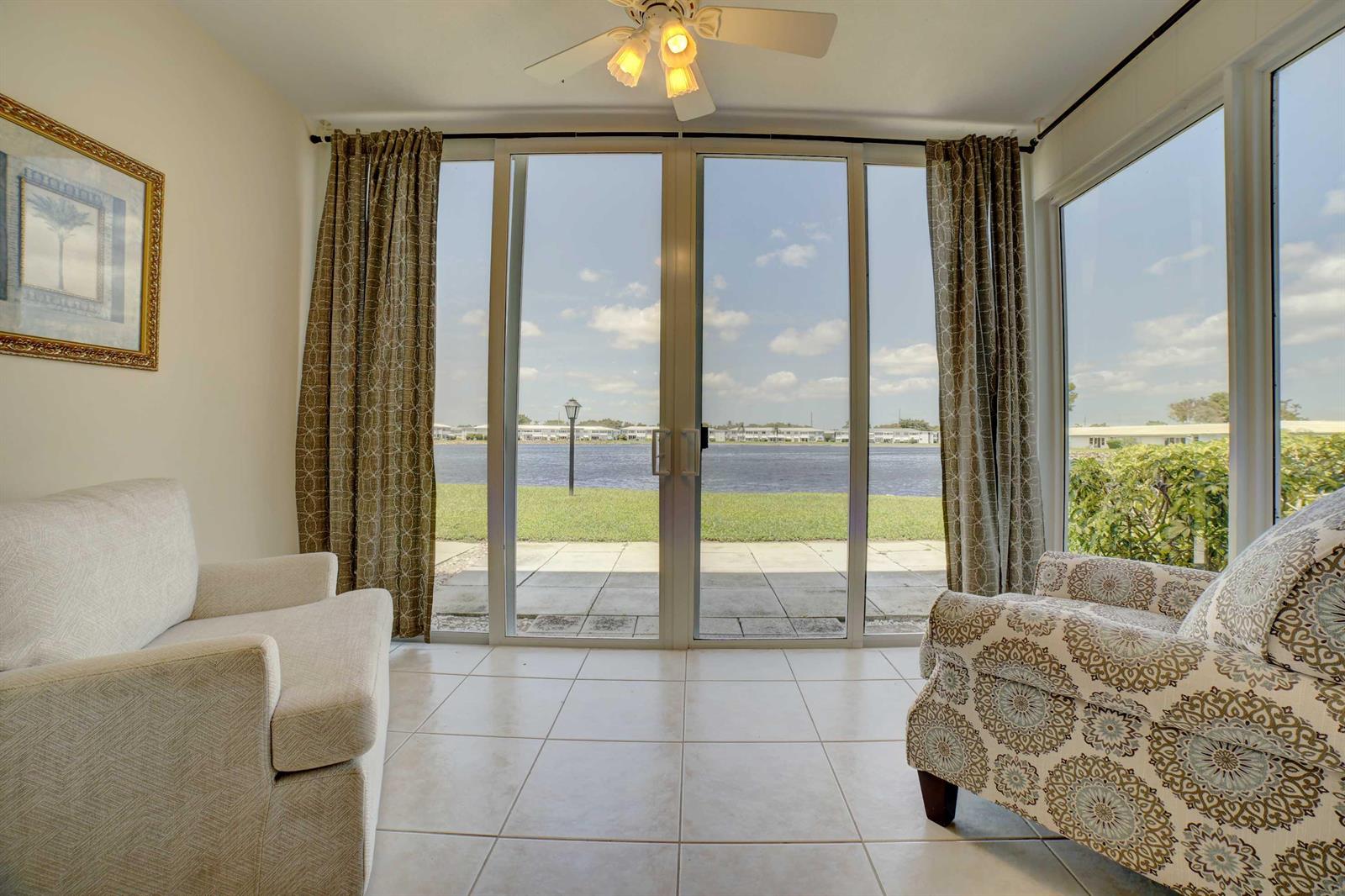 A sunroom with tile floors, two armchairs, and sliding glass doors overlooking a lake — 1801 Ocean Drive # 110, Boynton Beach FL 33426, BOYNTON BEACH, FL