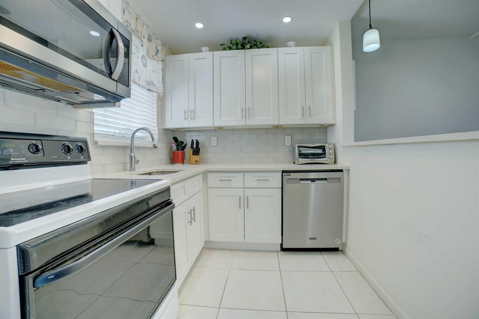 A kitchen features white cabinets, stainless steel appliances, a subway tile backsplash, and tile flooring — 1801 Ocean Drive # 110, Boynton Beach FL 33426, BOYNTON BEACH, FL