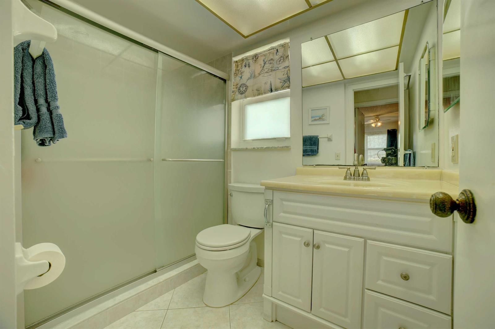 A bathroom features a glass-enclosed shower, a white vanity with a sink, and a toilet — 1801 Ocean Drive # 110, Boynton Beach FL 33426, BOYNTON BEACH, FL