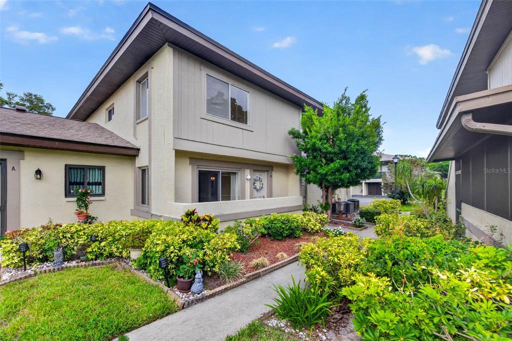 The exterior of a two-story residential building features light-colored siding, a concrete walkway, and landscaping — 2943 LICHEN LANE UNIT B, CLEARWATER, FL