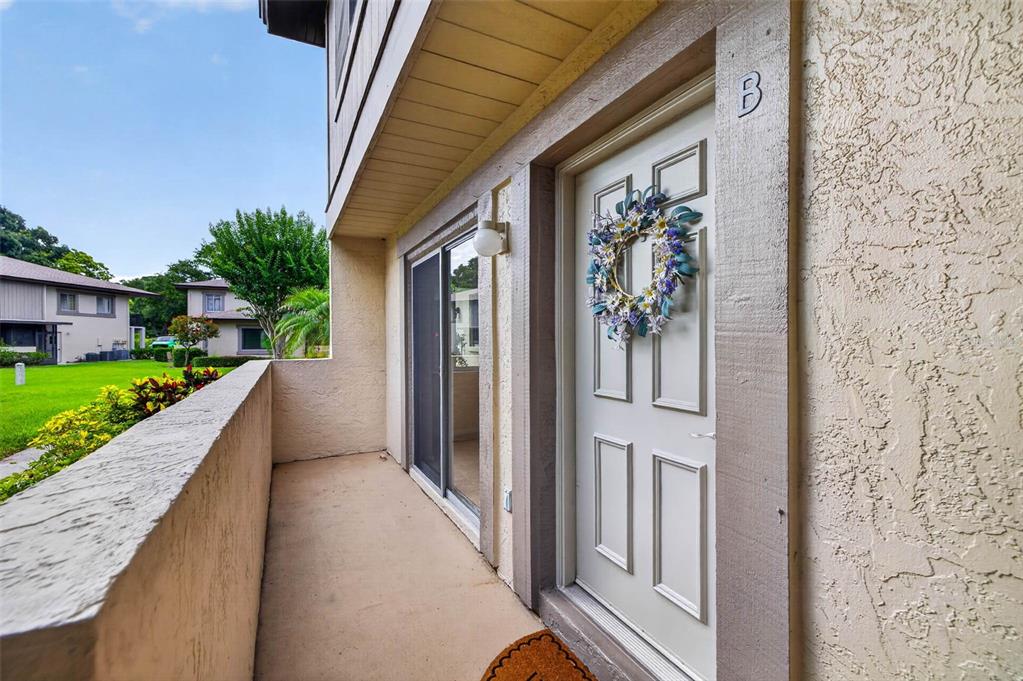 An exterior view of a covered balcony featuring a white front door and sliding glass door — 2943 LICHEN LANE UNIT B, CLEARWATER, FL