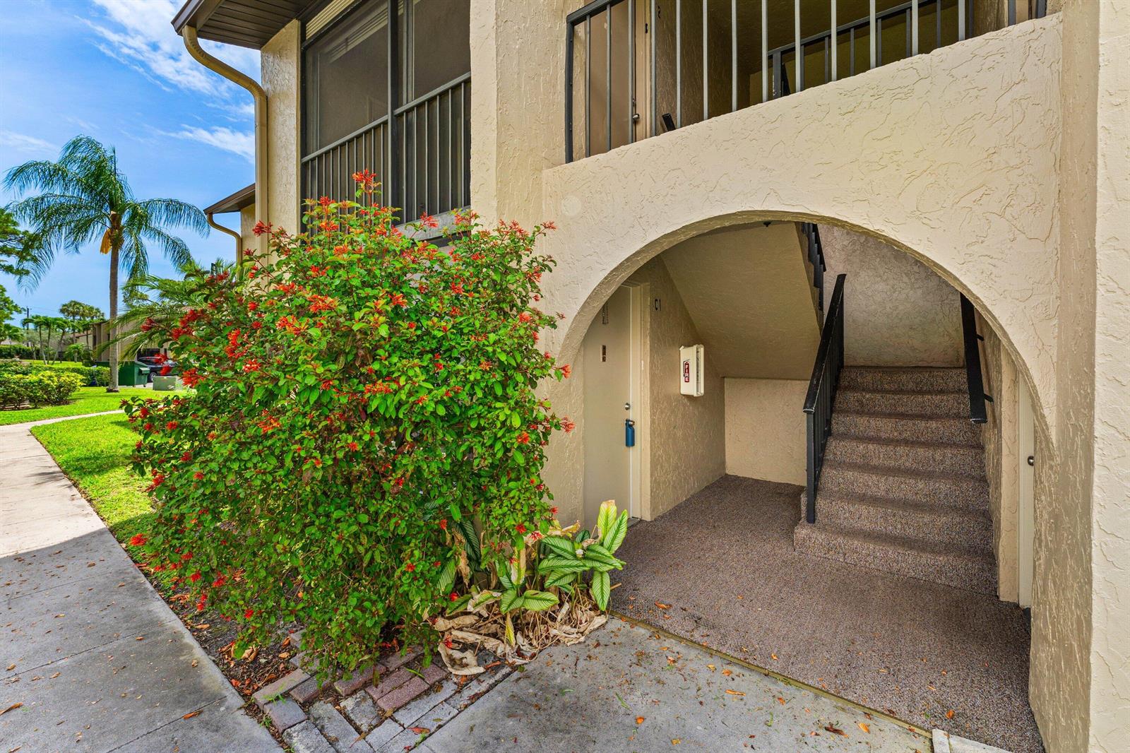 An exterior view of a tan building showing a ground-level entrance, stairs, and landscaping — 509 Shady Pine Way # C1, FL 33415, FL