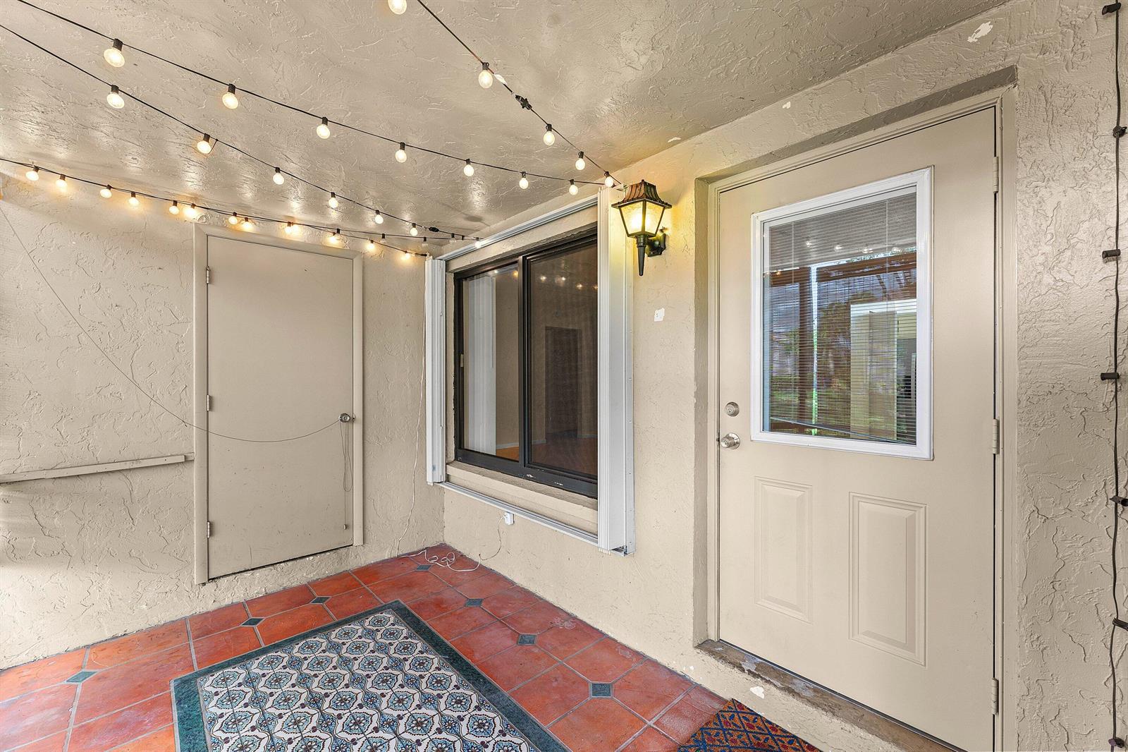 A covered patio with terracotta tile flooring, string lights, a window, and two exterior doors — 509 Shady Pine Way # C1, FL 33415, FL