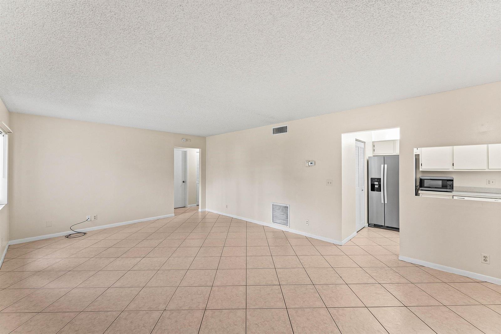 An empty living room with beige tile flooring and a pass-through window to the kitchen — 509 Shady Pine Way # C1, FL 33415, FL