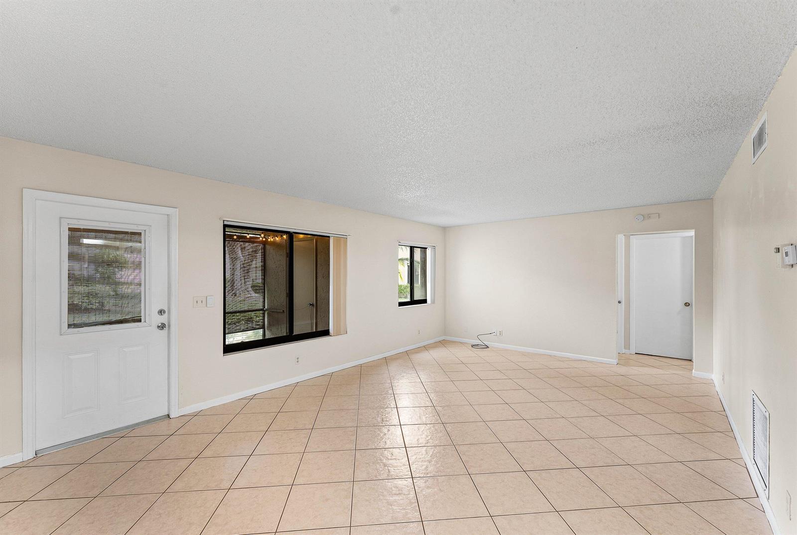 An empty room features beige tile flooring, light-colored walls, a white door, and two windows — 509 Shady Pine Way # C1, FL 33415, FL