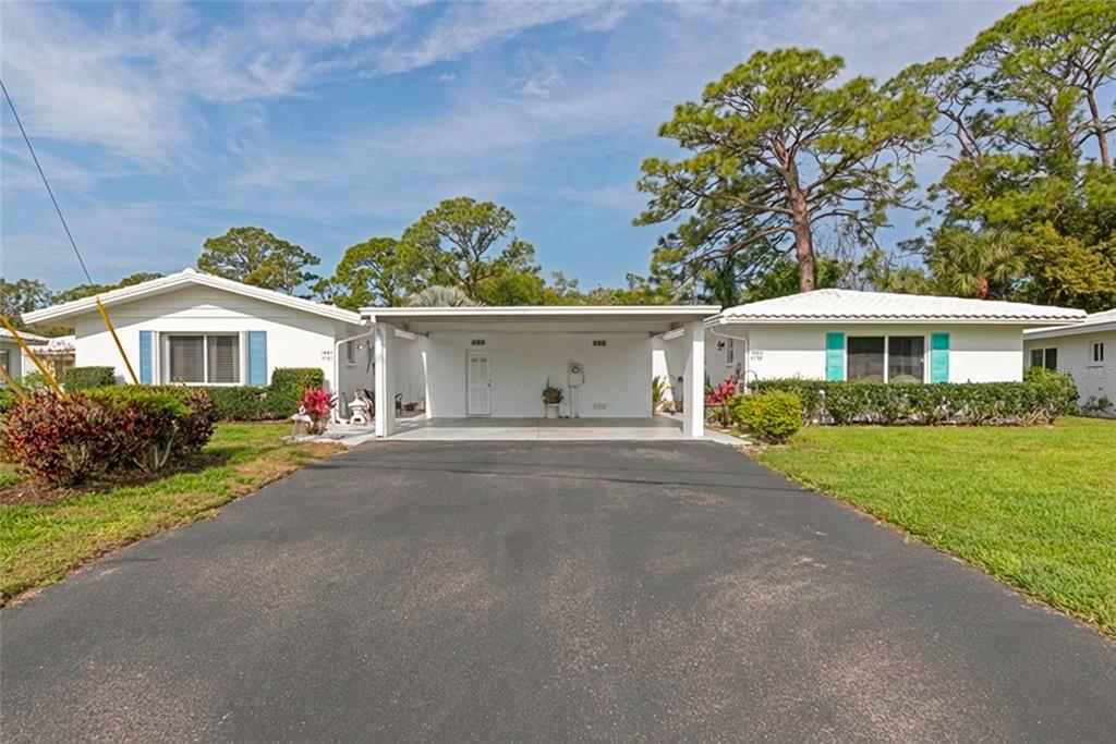 A single-story house with a central carport, asphalt driveway, and green lawn under a blue sky — 1807 UNIVERSITY PLACE UNIT 151, SARASOTA, FL