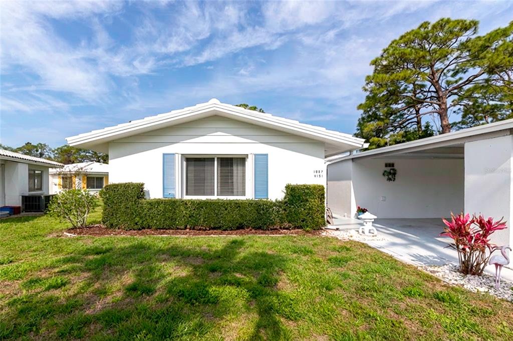 A white single-story house features blue shutters, a manicured hedge, and an attached carport — 1807 UNIVERSITY PLACE UNIT 151, SARASOTA, FL