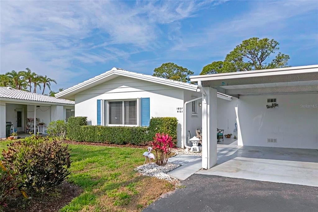 A white single-story house features blue shutters, a front lawn, and an attached carport — 1807 UNIVERSITY PLACE UNIT 151, SARASOTA, FL