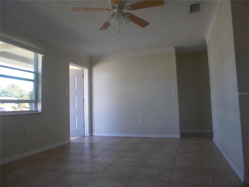 An empty room with beige tile flooring, a ceiling fan, and an open doorway — 5982 52ND AVENUE N, KENNETH CITY, FL