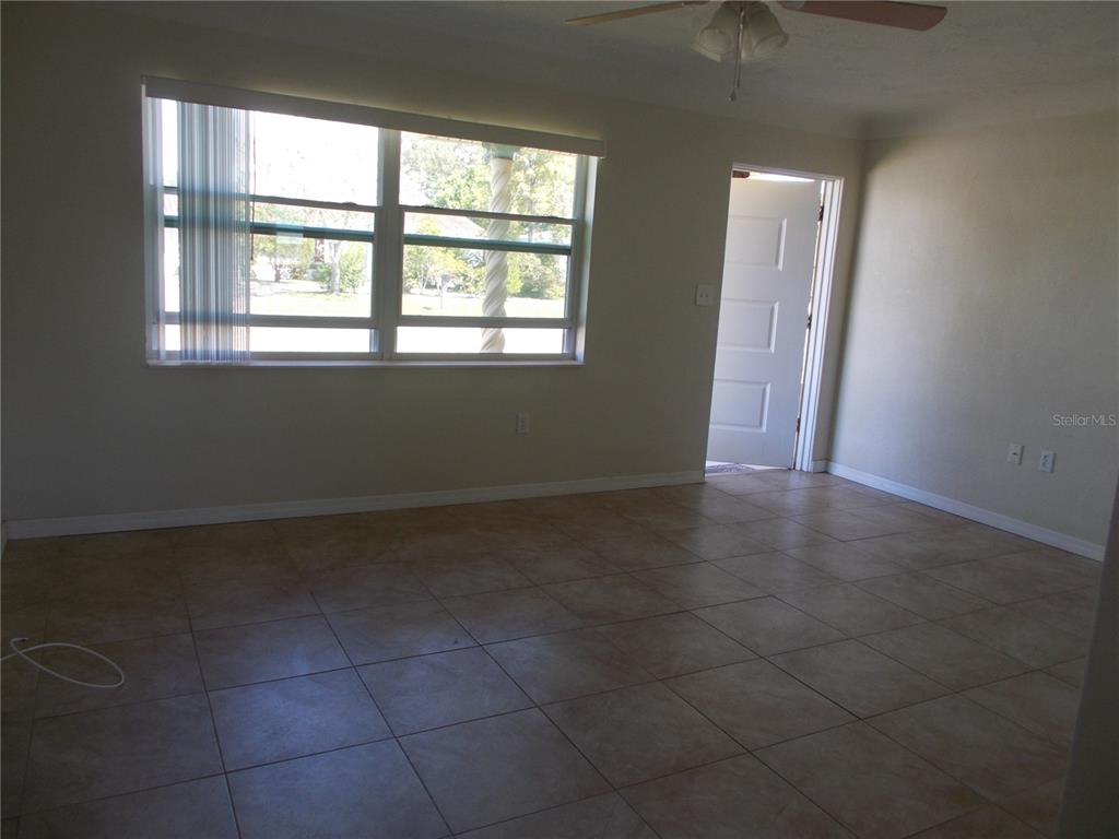 An empty room with beige tile flooring, a large window, and an open doorway — 5982 52ND AVENUE N, KENNETH CITY, FL