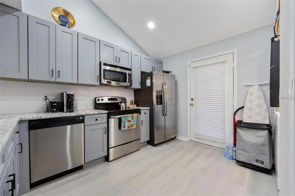 A kitchen with gray cabinets, stainless steel appliances, light wood-look flooring, and a glass-paned door — 3401 CYPRESS HEAD COURT, TAMPA, FL