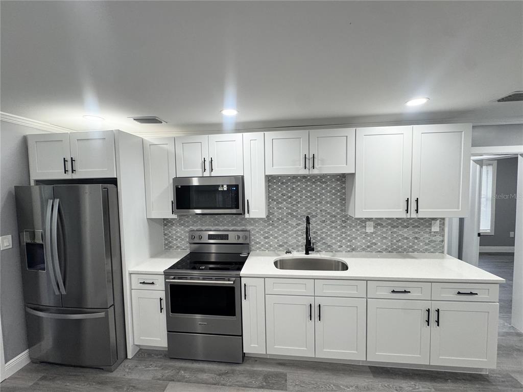 A modern kitchen features white cabinets, stainless steel appliances, and a gray patterned tile backsplash — 425 S OBSERVATORY DRIVE, ORLANDO, FL
