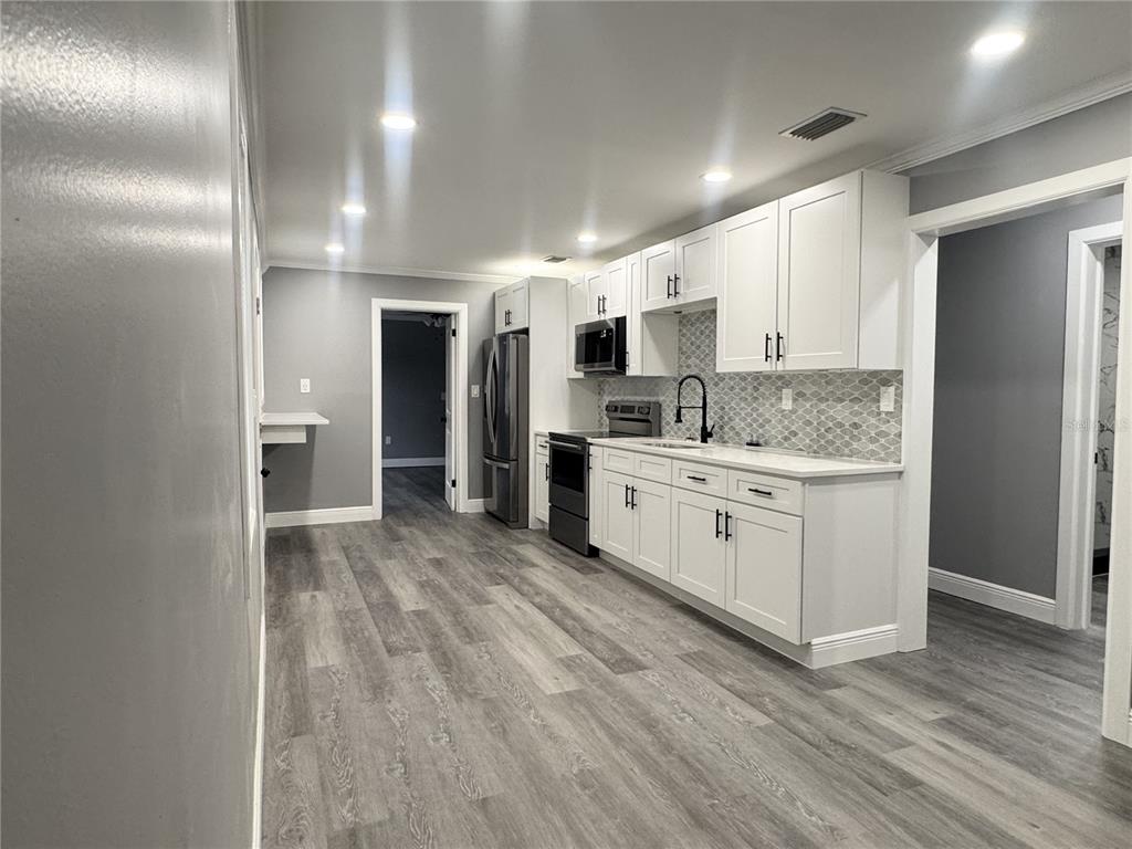 A kitchen features white cabinetry, stainless steel appliances, gray flooring, and a patterned tile backsplash — 425 S OBSERVATORY DRIVE, ORLANDO, FL