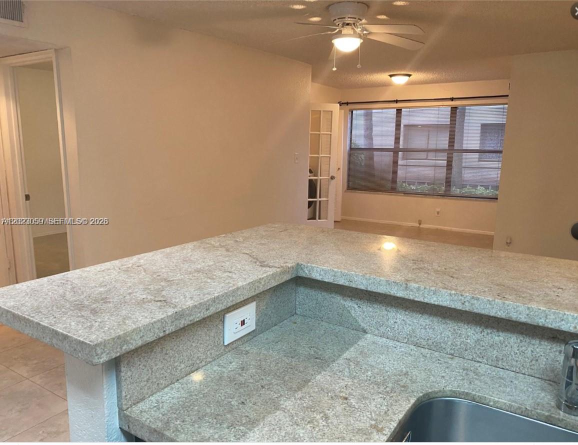 A kitchen counter with granite countertops overlooks a living area with a ceiling fan — 2946 S University Dr # 7110, Davie FL 33328, DAVIE, FL