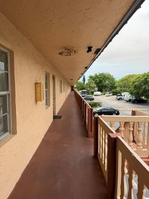 An exterior walkway with a tan stucco wall and a wooden railing overlooks a parking lot — 9272 SW 3rd Street # 409, Boca Raton FL 33428, BOCA RATON, FL