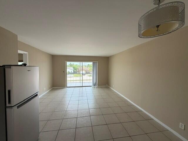 An empty room with beige walls, tile flooring, a refrigerator, and a sliding glass door — 9272 SW 3rd Street # 409, Boca Raton FL 33428, BOCA RATON, FL