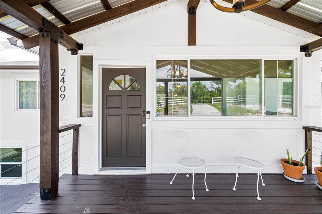 A covered wooden porch features a dark front door, white walls, and two metal chairs — 2409 LAKE TINY ROAD, DELTONA, FL