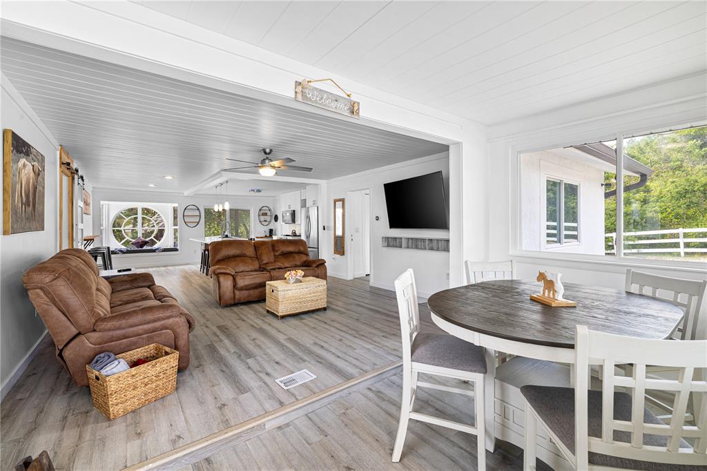 An open-concept living and dining area features wood-look flooring, white plank ceilings, and brown furniture — 2409 LAKE TINY ROAD, DELTONA, FL