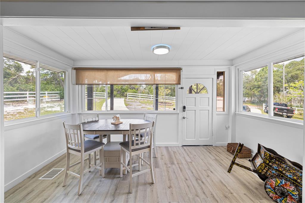 A sunroom with white walls, wood-look flooring, a dining set, and views of a yard — 2409 LAKE TINY ROAD, DELTONA, FL