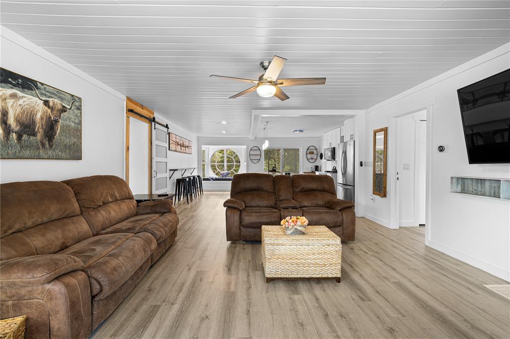 A living room features brown sofas, a wicker coffee table, and light wood-look flooring — 2409 LAKE TINY ROAD, DELTONA, FL