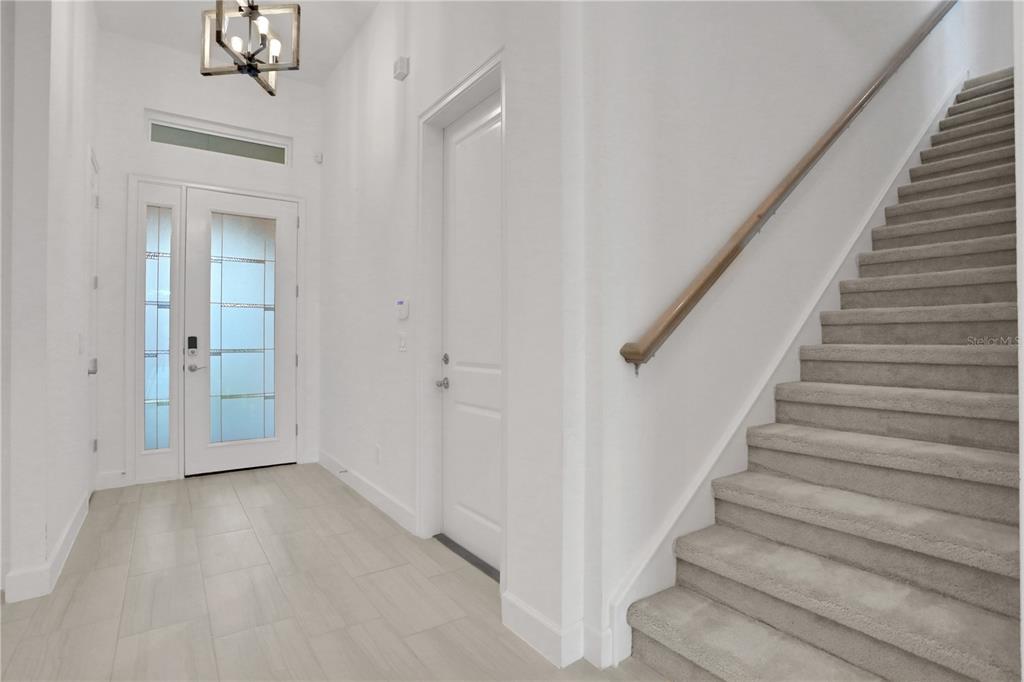 A bright entryway features light tile flooring, a white front door, and carpeted stairs — 6239 WOODHAVEN VILLAGE DRIVE, PORT ORANGE, FL