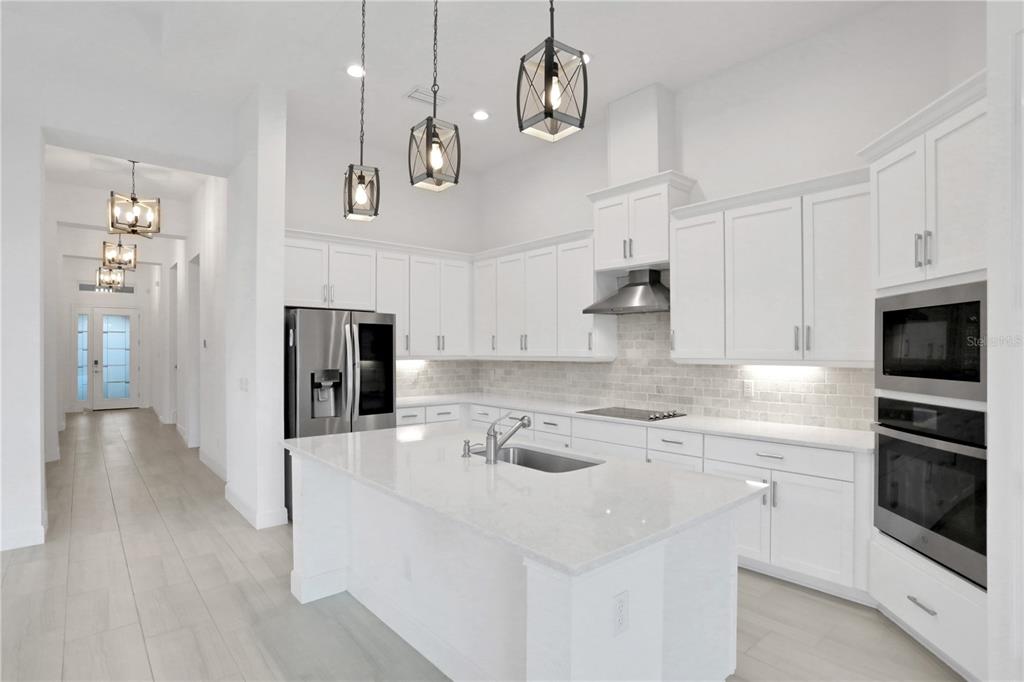 A modern white kitchen features a large island, stainless steel appliances, and hanging pendant lights — 6239 WOODHAVEN VILLAGE DRIVE, PORT ORANGE, FL