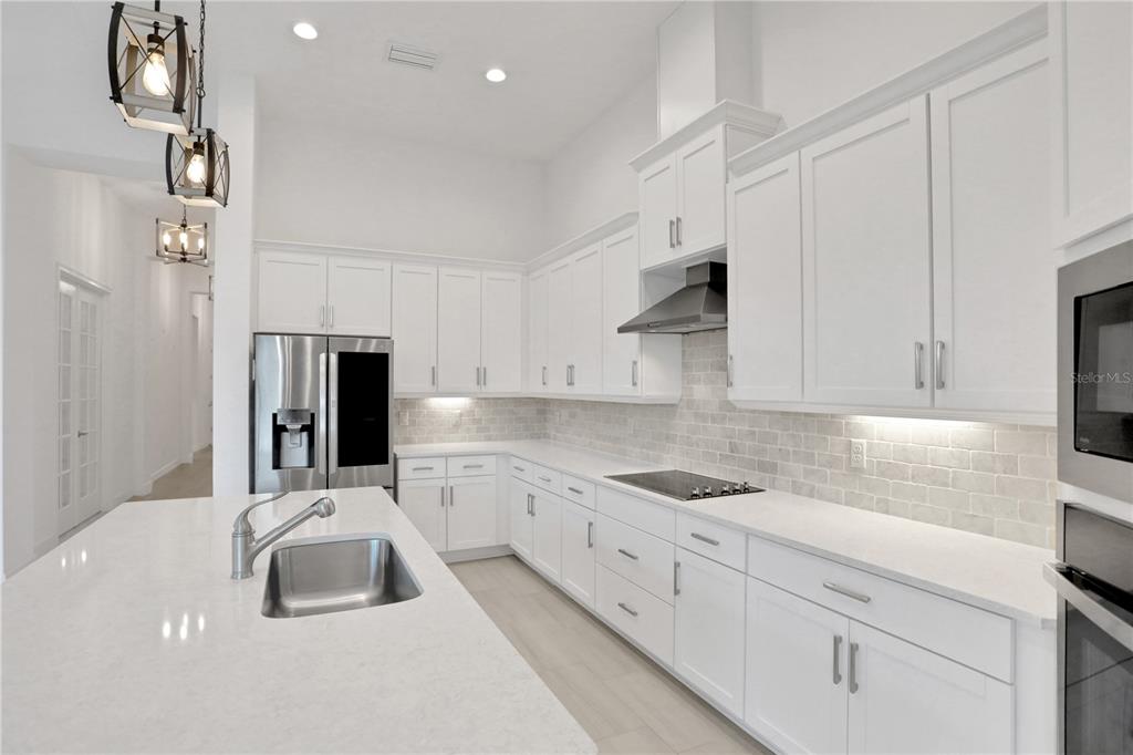 A modern kitchen features white cabinetry, quartz countertops, a stainless steel refrigerator, and pendant lighting — 6239 WOODHAVEN VILLAGE DRIVE, PORT ORANGE, FL