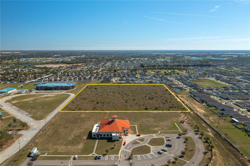 An aerial view shows a vacant rectangular lot outlined in yellow near a large building — 0 ORCHID DRIVE, HAINES CITY, FL