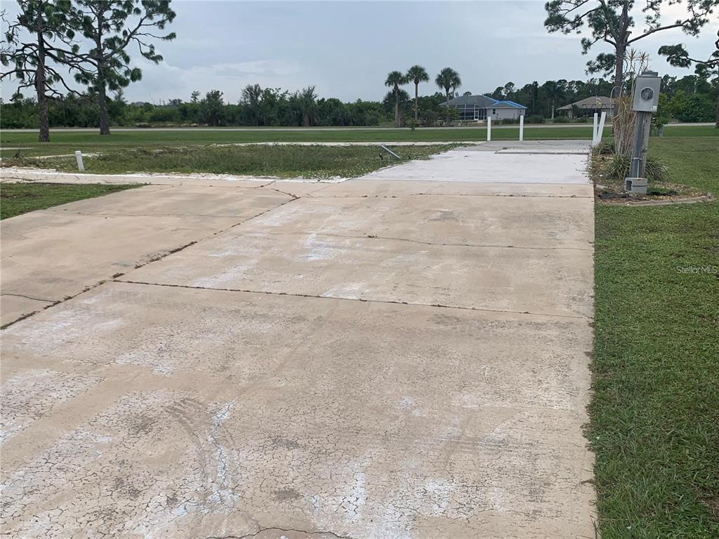 A concrete driveway leads to a vacant lot with a utility pole and distant houses — 7540 DANVERS CIRCLE, PORT CHARLOTTE, FL
