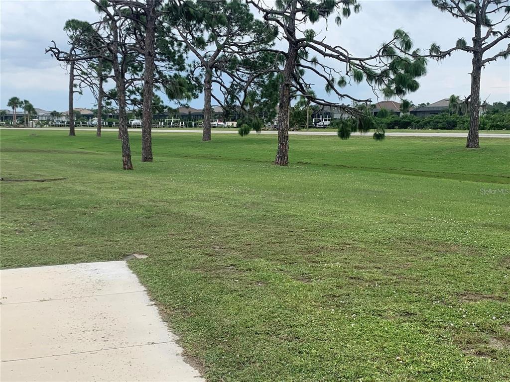 A grassy lawn with several pine trees leads to a road and residential houses — 7540 DANVERS CIRCLE, PORT CHARLOTTE, FL