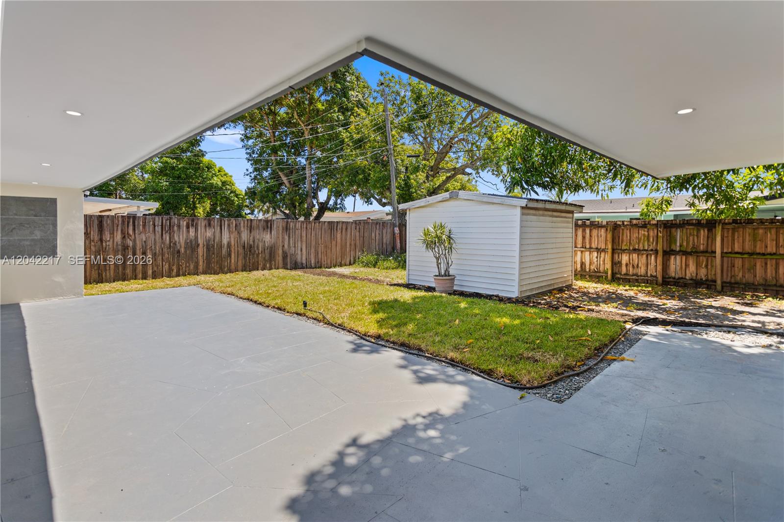 A paved patio overlooks a grassy backyard with a white shed and wooden fence — 2431 Sabal Palm Dr, Miramar FL 33023, MIRAMAR, FL