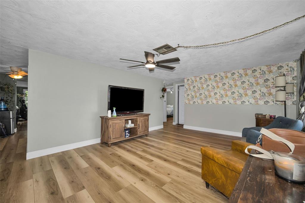 A living room features wood-look flooring, a floral accent wall, and a dark green front door — 3541 BIGELOW DRIVE, HOLIDAY, FL