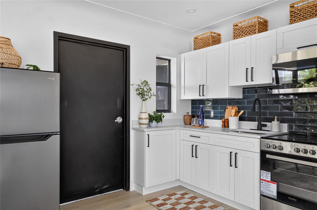 A kitchen features white cabinets, a dark tiled backsplash, stainless steel appliances, and a black door — 600 COREY AVENUE, ST PETE BEACH, FL
