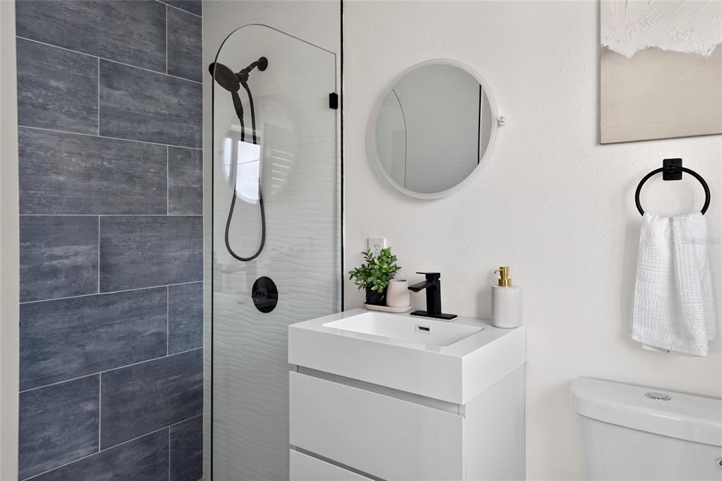 A modern bathroom features a white vanity, a round mirror, and a glass-enclosed shower — 600 COREY AVENUE, ST PETE BEACH, FL