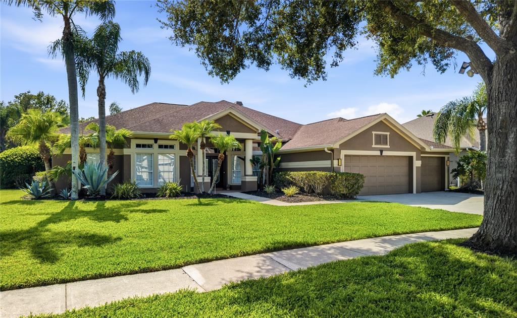 A single-story suburban house with a brown exterior, a three-car garage, and a manicured lawn — 5522 REFLECTIONS BOULEVARD, LUTZ, FL