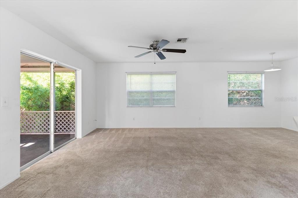 A carpeted living room features a ceiling fan, two windows, and a sliding glass door — 9410 TACOMA AVENUE UNIT A, ENGLEWOOD, FL