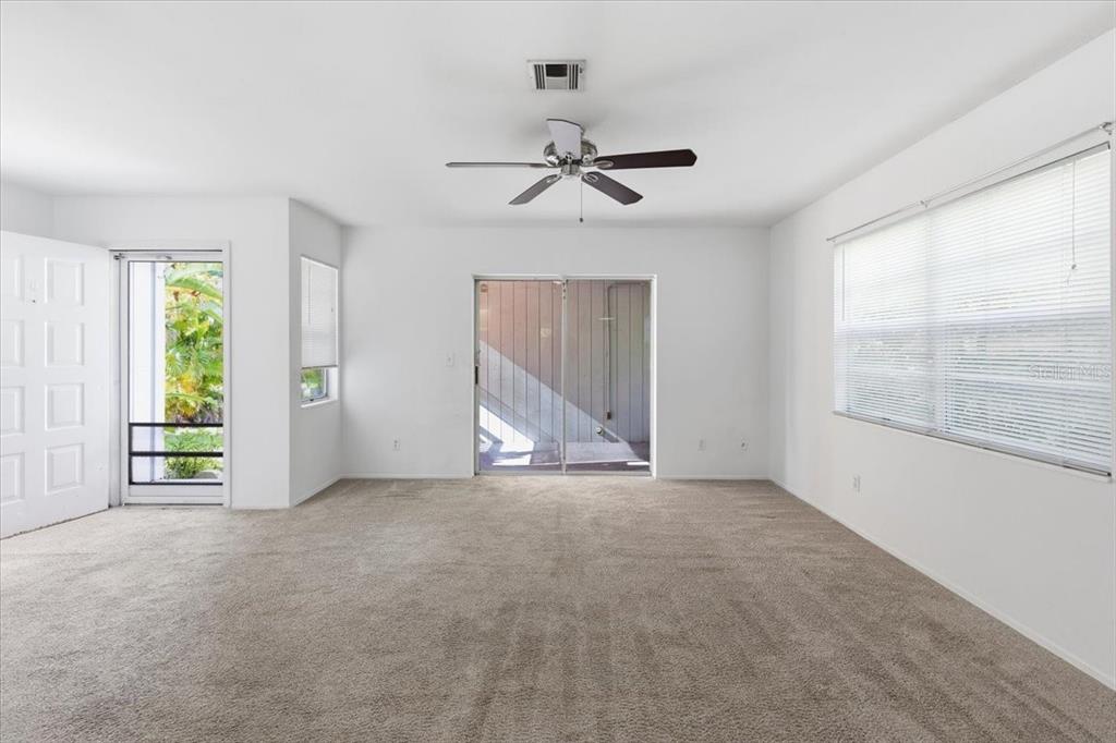 A carpeted living room features a ceiling fan, a sliding glass door, and a screen door — 9410 TACOMA AVENUE UNIT A, ENGLEWOOD, FL